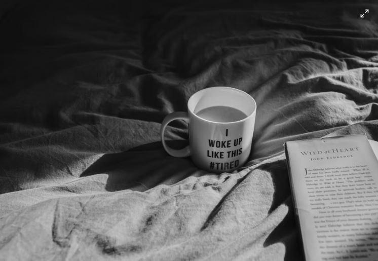 A mug of coffee and an open book on a bed