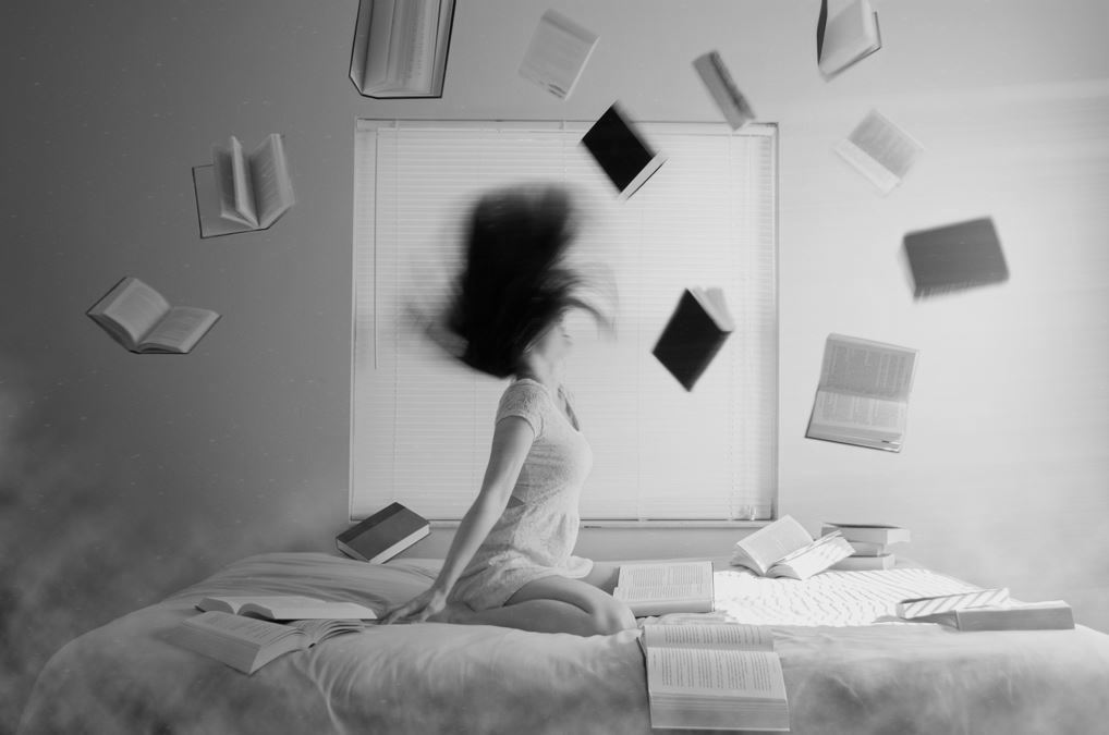 Woman sitting on a bed with books flying around